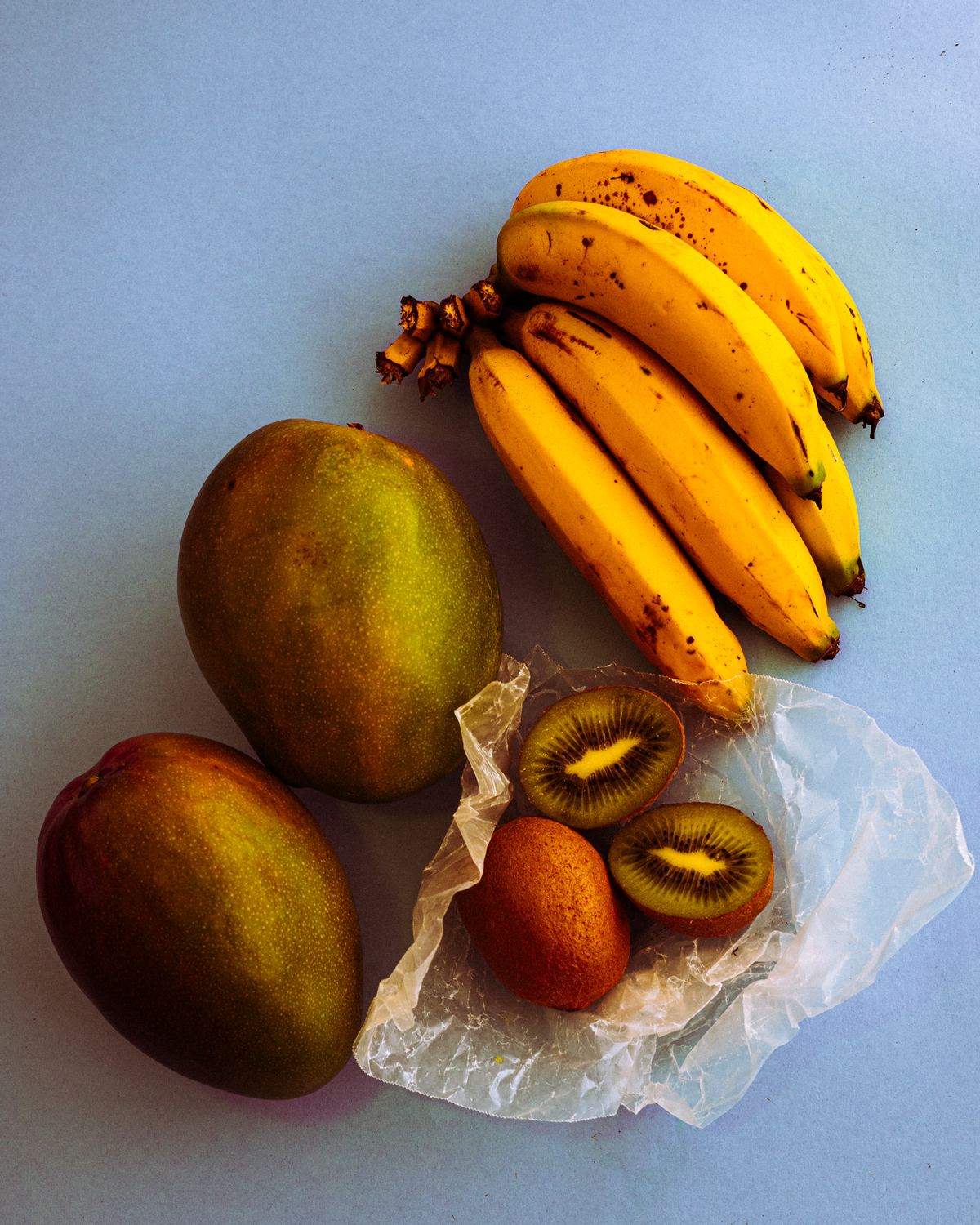 Bodegón de plátanos, mangos y kiwis sobre fondo azul