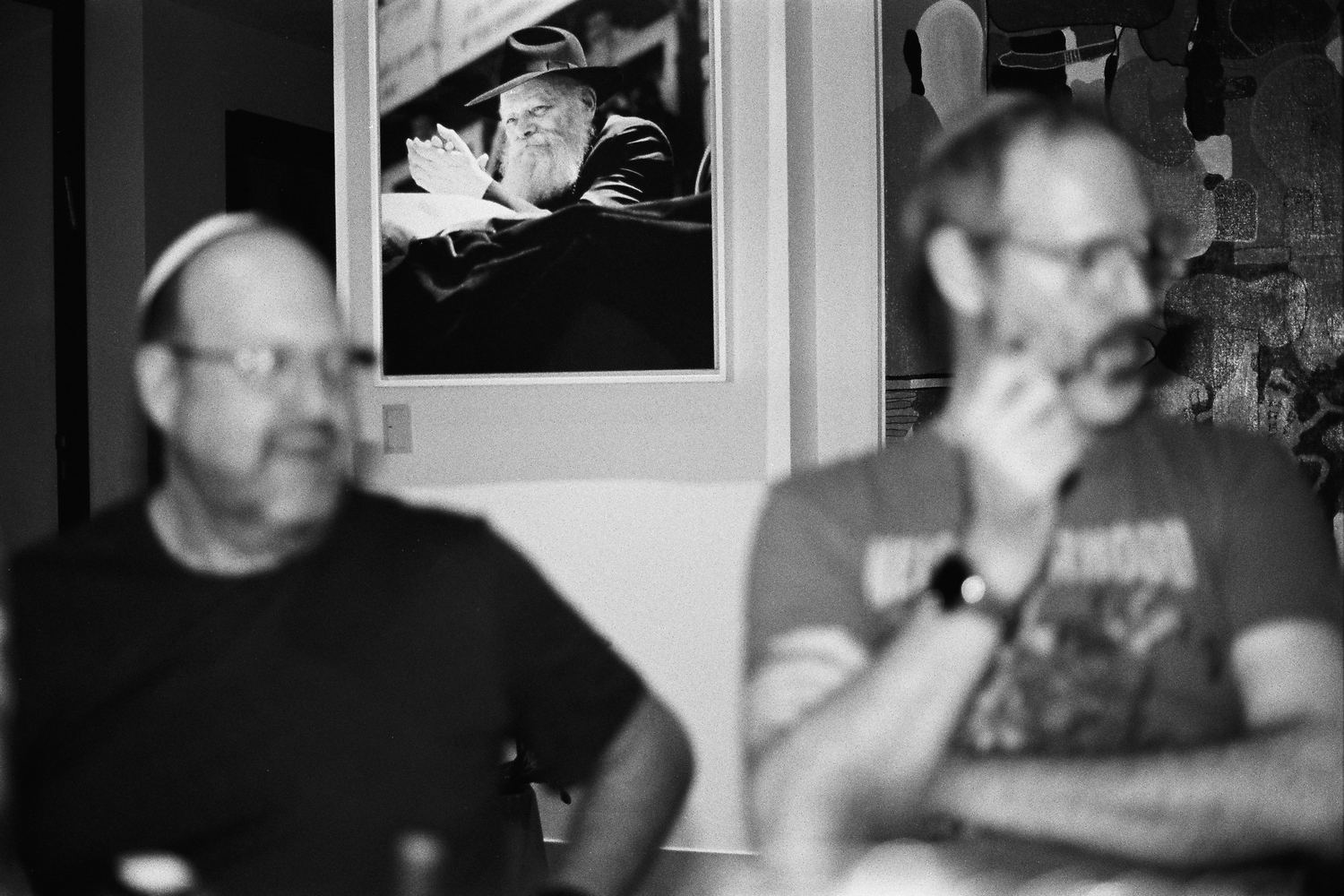 Dos hombres conversando bajo un retrato del Rebe