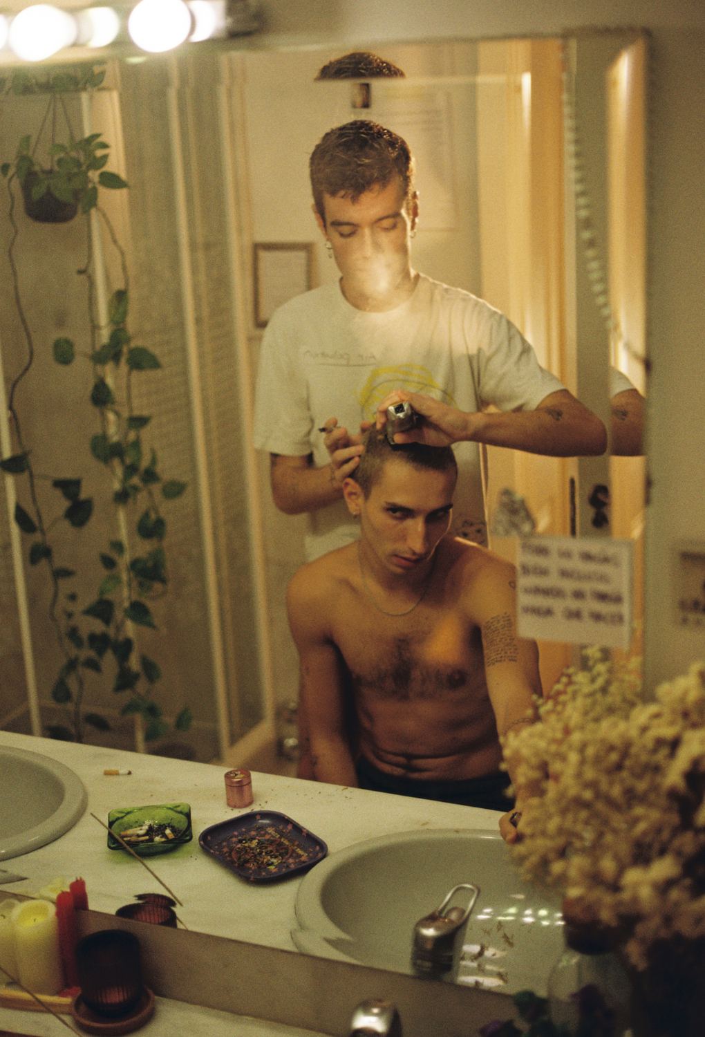 Un chico decolora el pelo de otro frente al espejo