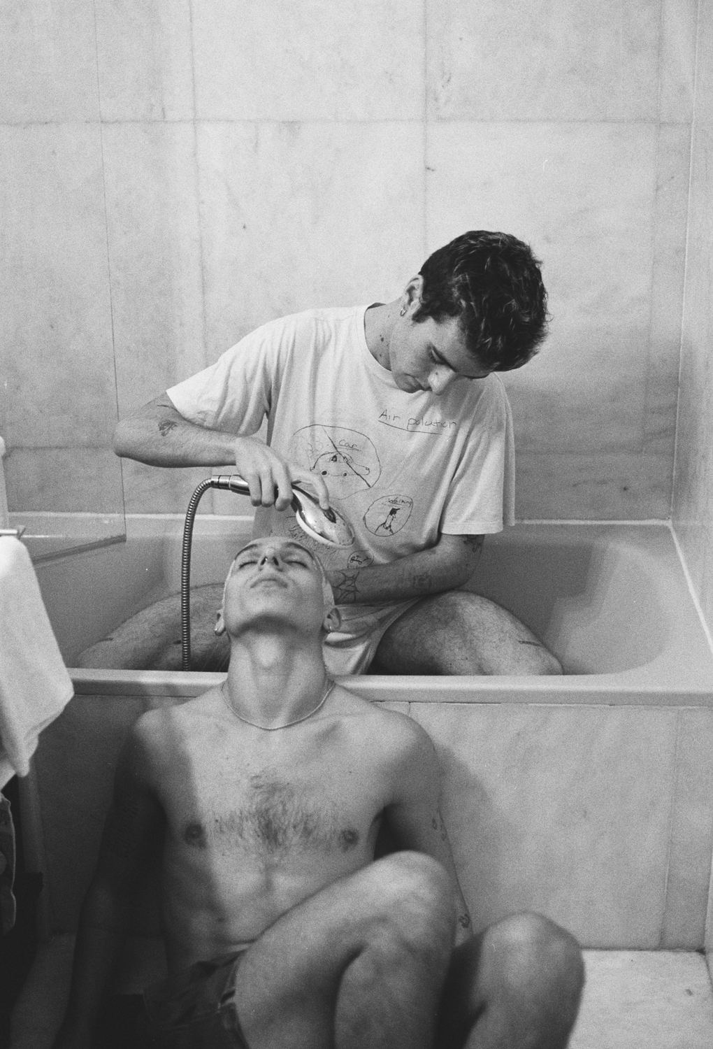 Un chico enjuaga el pelo de otro en la bañera